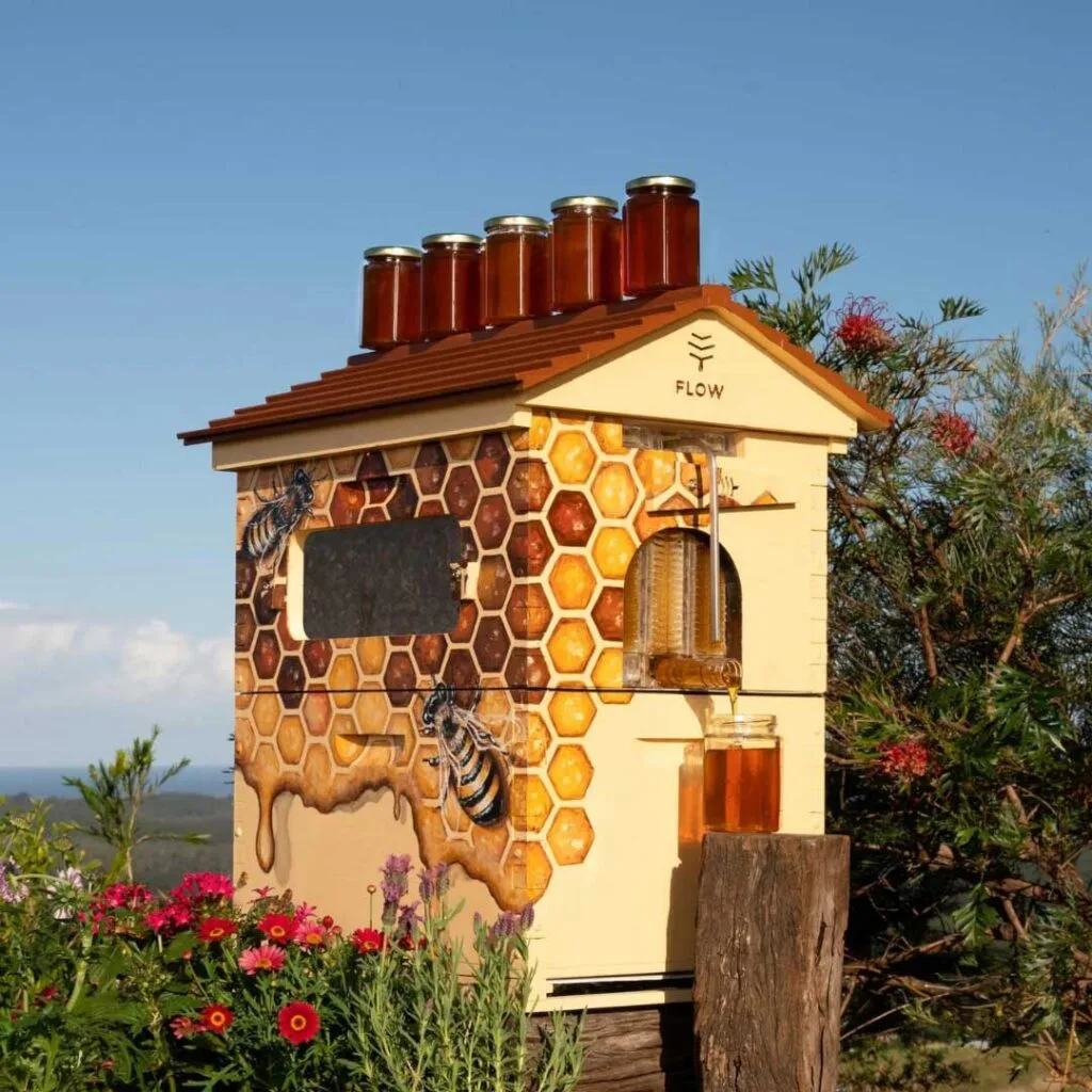 A Flow bee hive sitting in a country setting with jars of honey around it.