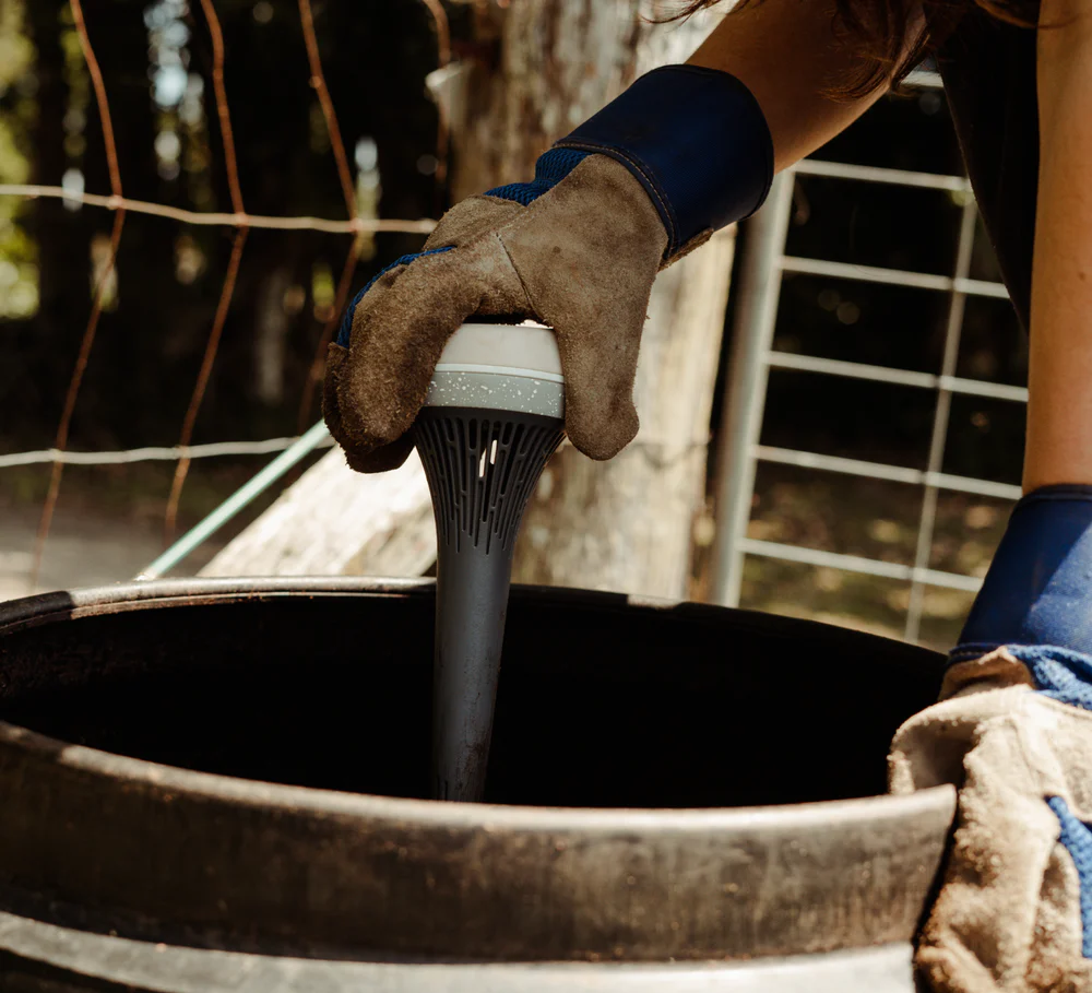 A smart compost monitor being placed into a compost bin by a gardener wearing garden gloves.