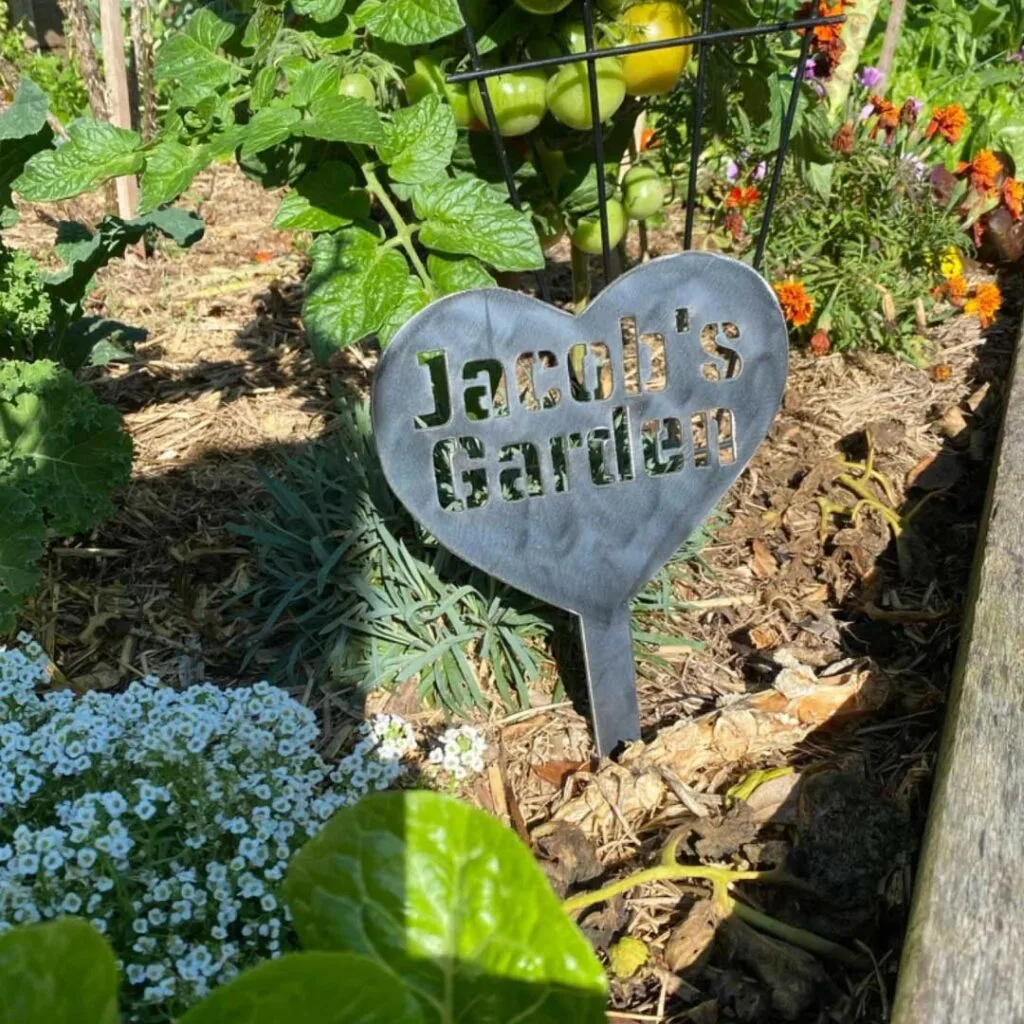 A Personalised Metal Garden Sign in a garden bed with flowers and tomatoes.